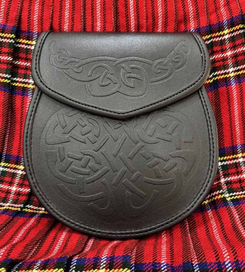 Peut inclure: Un sporran en cuir noir avec un motif de n&oelig;uds celtiques en relief. Le sporran est dot&eacute; d'une fermeture &agrave; rabat et est pr&eacute;sent&eacute; sur un fond &agrave; carreaux rouges et noirs. Accessoire &eacute;cossais traditionnel.