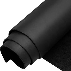 May include: A roll of solid black leather featuring a smooth, matte surface on the exterior and a textured, fibrous underside. The material is coiled into a cylindrical shape, showcasing the thickness and consistent dark color of the hide.