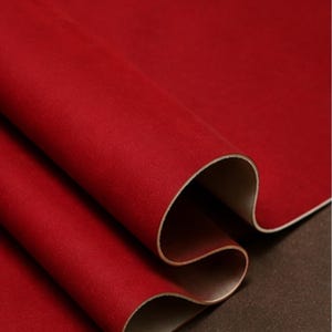 May include: Close-up of a rolled sheet of red material with a textured surface. The underside of the material is a light tan color. The material is layered, revealing the contrasting colors and textures.