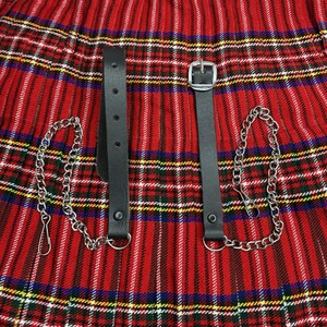 Peut inclure: Jupe pliss&eacute;e &agrave; carreaux rouges avec des lani&egrave;res en cuir noir et des cha&icirc;nes argent&eacute;es. La jupe pr&eacute;sente un motif tartan classique avec des rayures rouges, blanches, jaunes et bleues. Les lani&egrave;res ont des boucles et des rivets argent&eacute;s.