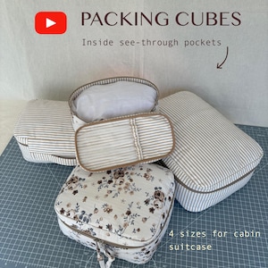 May include: Four packing cubes in various sizes, with striped and floral patterns. The cubes have brown trim and zippers. The text on the image reads "PACKING CUBES" and "4 sizes for cabin suitcase."