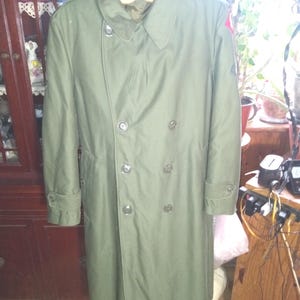 May include: A white ceramic mug with a black handle and the text "But First, Coffee" in a bold, black font. The mug is set against a blurred background, suggesting a cozy setting. The mug appears to be approximately 4 inches tall.