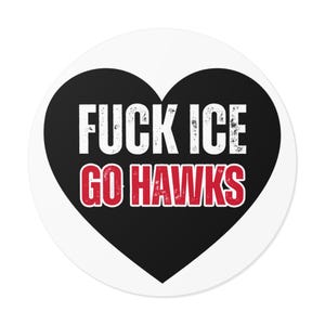 May include: Round sticker with a black heart shape. The sticker has the words "FUCK ICE" in white, and "GO HAWKS" in red, with a distressed font. The sticker is on a white background.
