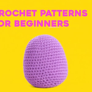 May include: A purple crocheted egg shape against a bright yellow background. The text "CROCHET PATTERNS FOR BEGINNERS" is displayed in pink above the egg. The image is well-lit and the colors are vibrant.