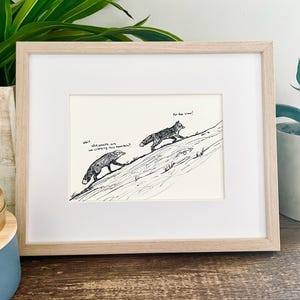 以下が含まれることがあります： 山を登る2匹のキツネが描かれた、紙に黒インクのモノクロ画。額縁入り。下のキツネが「Wait, why exactly are we climbing this mountain?」と尋ね、上のキツネが「For the view!」と答える様子が描かれている。明るい色の木製フレーム。