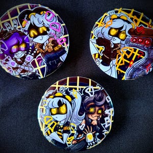 May include: Three round pinback buttons featuring anime-style characters with yellow and purple accents. The buttons have a dark background with a grid pattern. Each button displays a different character design, with varying expressions and outfits.