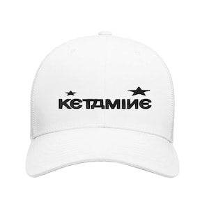 Op de afbeelding: Witte truckerpet met een gebogen klep en mesh achterkant. De voorkant toont het woord "KETAMИИE" in vette zwarte letters, met aan weerszijden een ster. Een casual accessoire.