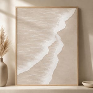 Puede incluir: Una impresión de arte mural rectangular en un marco de madera clara que muestra una vista aérea de una playa de arena con olas blancas del océano llegando a la orilla. La paleta de colores consiste en tonos beige, arena y blanco suaves.