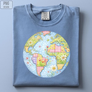 May include: A light blue t-shirt with a colorful Earth graphic. The Earth design features patchwork continents with floral and gingham patterns. The shirt has a crew neck and the Comfort Colors brand tag.