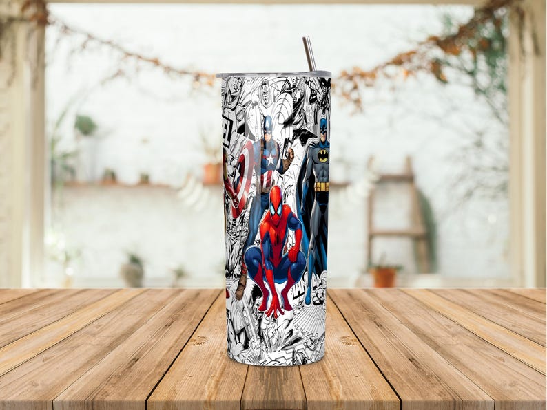 K&ouml;nnte beinhalten: Ein Edelstahlbecher mit einem Comic-Design, das verschiedene Superhelden zeigt, darunter Spider-Man, Captain America und Batman. Der Becher hat einen silbernen Deckel und einen Strohhalm. Der Hintergrund zeigt ein Fenster und einen Holztisch.