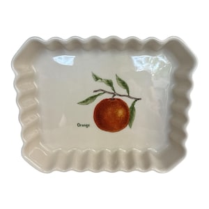 Könnte beinhalten: Cremefarbene rechteckige Servierplatte mit gerüschtem Rand. In der Mitte befindet sich eine Aquarellillustration einer Orange auf einem Zweig mit grünen Blättern. Das Wort "Orange" ist darunter gedruckt.