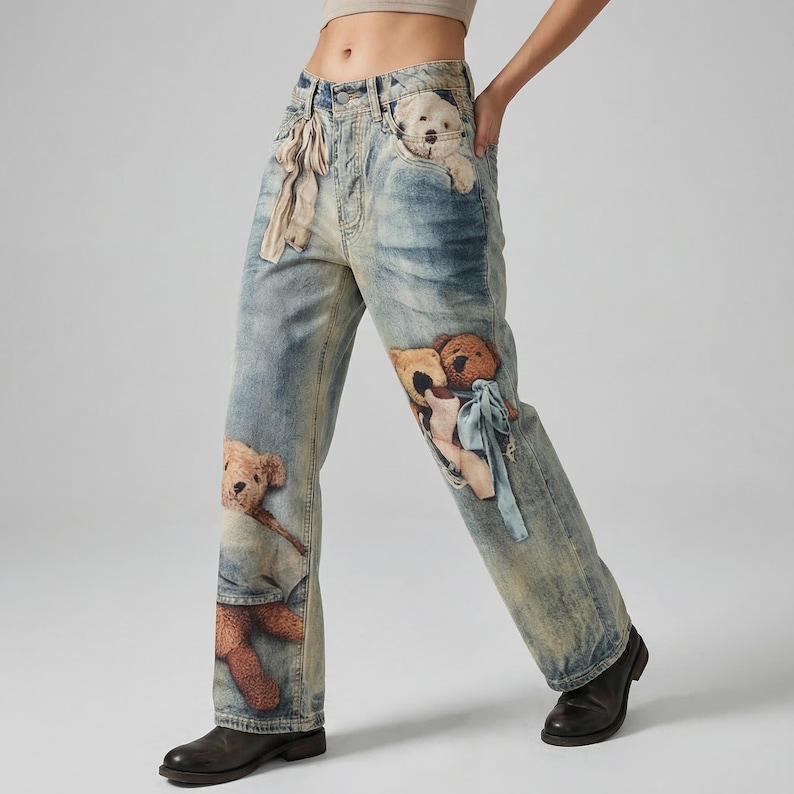 May include: Light blue denim jeans with a faded wash and multiple teddy bear appliqu&eacute;s. The jeans have a relaxed fit, with a teddy bear peeking out of the front pocket and others on the legs. The jeans are worn with black shoes.