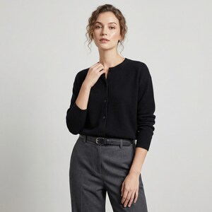 May include: A black cardigan with a round neckline and button closure. The cardigan is paired with gray trousers and a black belt. The outfit is simple and classic, suitable for various occasions.