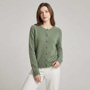 May include: A sage green cardigan with a round neckline and button-down front. The long-sleeved sweater is made of a soft material and is paired with white pants. The cardigan is a versatile piece for layering.