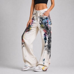Op de afbeelding: Off-white denim jeans met een wijde pijp en een hoge taille. De jeans zijn bespat met kleurrijke verf in tinten blauw, rood, geel en zwart. Voorzien van twee voorzakken en twee cargozakken.