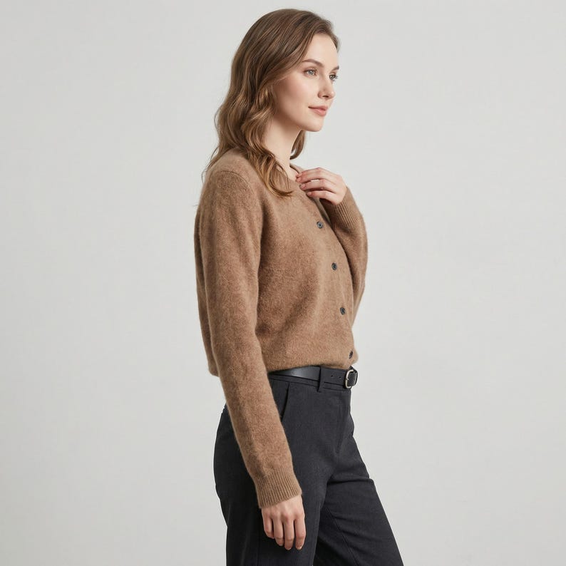 May include: A light brown cardigan with long sleeves and a button-up front. The cardigan is paired with dark gray pants and a black belt. The outfit is simple and classic.
