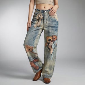 May include: Light blue denim jeans with a faded wash and a relaxed fit. The jeans feature multiple teddy bear appliqu&eacute;s in shades of brown and tan. A beige ribbon is tied at the waist. The jeans are worn with brown leather shoes.