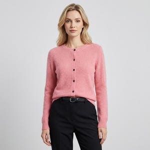 May include: A light pink cardigan with long sleeves and a round neckline. The cardigan has black buttons down the front and is paired with black pants and a black belt. The outfit is simple and classic.