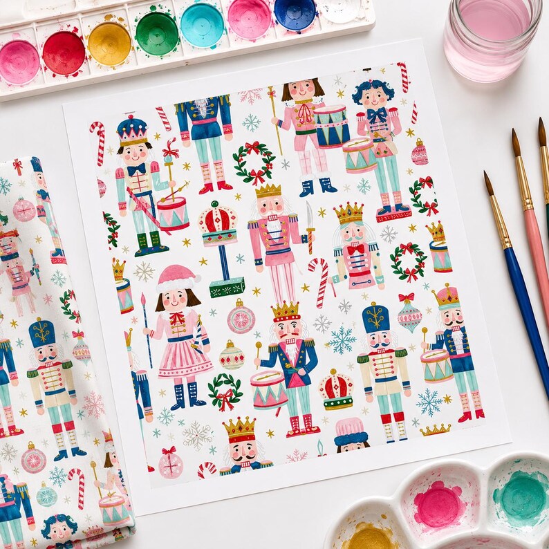 May include: A white paper sheet featuring a repeating watercolor pattern of nutcracker figures, crowns, wreaths, candy canes, and ornaments in shades of pink, blue, red, and green, surrounded by paintbrushes and watercolor paint palettes.