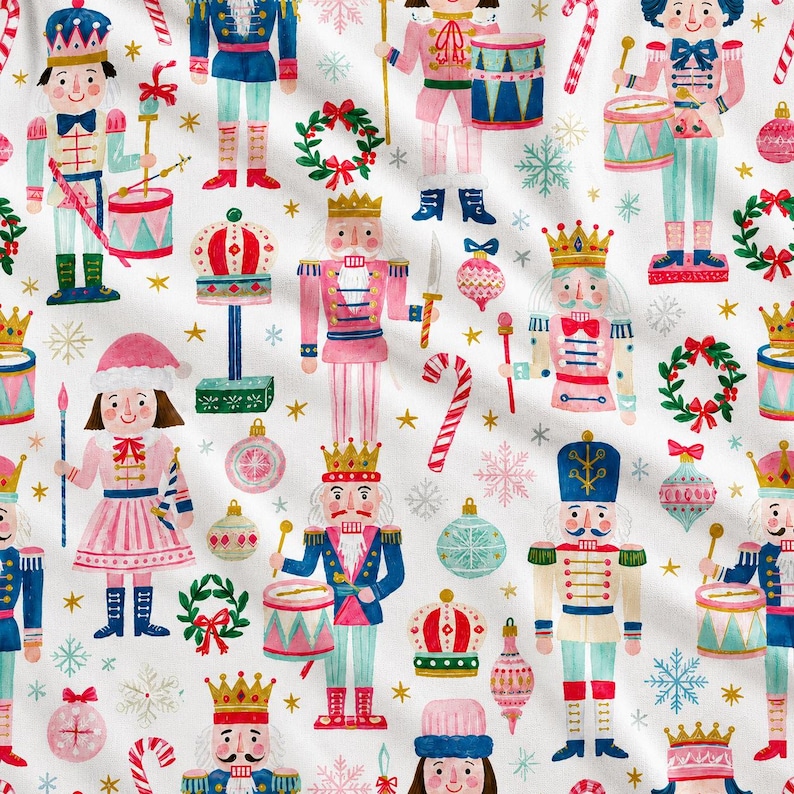 May include: A white fabric featuring a repeating pattern of watercolor-style nutcrackers in pink, blue, and red uniforms, interspersed with Christmas ornaments, candy canes, green wreaths, and gold stars on a clean white background.