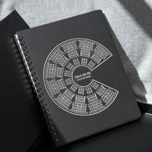 May include: Black spiral-bound notebook with a white graphic design and the text "CHALK AND INK A YEAR IN WINE NOTES". The notebook is open, revealing the spiral binding and a portion of the interior pages.