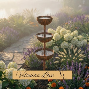 May include: A three-tiered outdoor water fountain with a weathered, rustic finish. Water cascades from the top bowl to the bottom. The fountain is set amidst lush greenery, including lavender and white hydrangeas. The text "Velonias Love" is at the bottom.