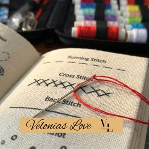 Könnte beinhalten: Nahaufnahme eines Nähsets mit einer Nadel, die mit rotem Faden versehen ist und eine Stoffprobe durchsticht. Der Stoff zeigt Beispiele für den Steppstich, den Kreuzstich und den Rückstich. Der Text "Velonias Love" steht auf einem goldenen Banner.