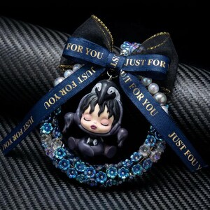 May include: A decorative ornament featuring a figurine of a person in a penguin costume, surrounded by a blue floral wreath and a black bow with gold trim. The blue ribbon has the text "JUST FOR YOU".