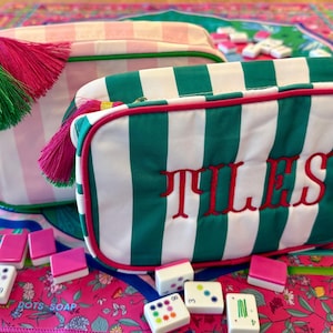 May include: Two rectangular cosmetic bags with tassels and the word "TILES" embroidered on one. One bag is pink and white striped, the other is green and white striped. Mahjong tiles are scattered around the bags.