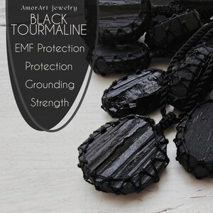 Close-up of multiple raw oval and round Black Tourmaline in deep black shades, resting on a white wood surface. The Black Tourmaline dark gemstone has strong parallel vertical striations, rough uneven edges, and a matte to slightly reflective texture with natural ridges and layered surfaces. Each piece is wrapped in a black macrame net and attached to a black cord with an adjustable knot closure. The image includes the text “Black Tourmaline, EMF Protection, Protection, Grounding, Strength”.