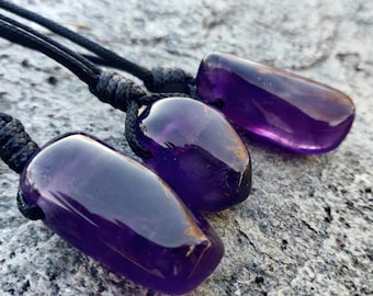 May include: Three polished amethyst pendants with black cords. The purple gemstones have a smooth, rounded shape. The image includes the text "No Extra Duties Upon Delivery".