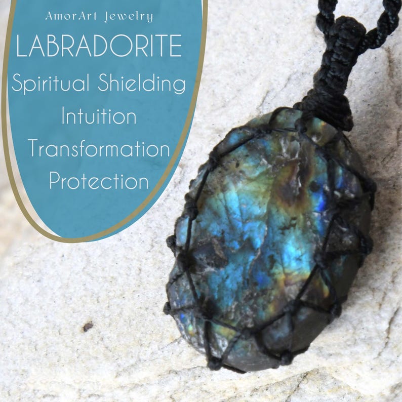 **Alt text:**

Raw Labradorite pendant with vivid blue, turquoise, and golden flashes shimmering across its natural rough surface, hand-wrapped in a black macrame net and suspended from an adjustable black cord. Displayed on a light stone background beside a blue information panel. Text on the image reads: **"Labradorite"**, **"Spiritual Shielding," "Intuition," "Transformation,"** and **"Protection."**