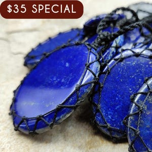 May include: Close-up of several deep blue lapis lazuli pendants, each encased in a black woven net. The pendants have a polished, smooth surface with natural variations. The text "$35 SPECIAL" is in a brown banner.