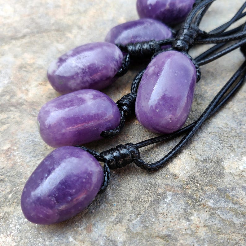 May include: Six polished, oval-shaped purple amethyst pendants strung on black cords. The amethyst stones have a smooth, glossy finish and vary slightly in shade. The cords are knotted at the top of each stone.