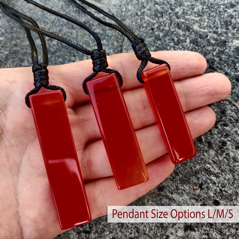 May include: Three rectangular, polished red pendants on black cords. The pendants are displayed against a neutral background. The text "Pendant Size Options L/M/S" is visible at the bottom of the image. These pendants are suitable for necklaces.