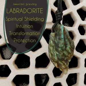 Close-up of a raw irregular Labradorite in shades of green, teal, and golden brown, displayed against a carved light stone background. The Labradorite gemstone has a natural rough texture with strong iridescent flashes, visible striations, and layered color play with reflective highlights. It is secured with a top knot and attached to a black cord with adjustable knot closure. The image includes the text "Labradorite Spiritual Shielding Intuition Transformation Protection".