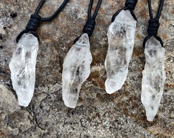 May include: Four clear quartz crystal pendants on black cords. The crystals are irregularly shaped and appear translucent. The cords are knotted at the top. The background is a rough, textured surface. Text at the bottom reads "No Extra Duties Upon Delivery."