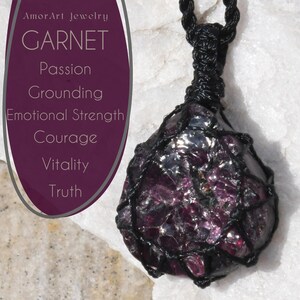 Close-up of a raw garnet crystal pendant in deep burgundy, plum, and near-black tones, displayed on a white crystal background. The natural gemstone features sparkling crystal faces, translucent sections, and rich flashes of red and purple visible within its rough organic structure. Text on the image reads: Garnet – Passion, Vitality, Grounding, Emotional Strength, Courage, and Truth. The pendant is secured in a black macrame net and attached to a black adjustable cord.