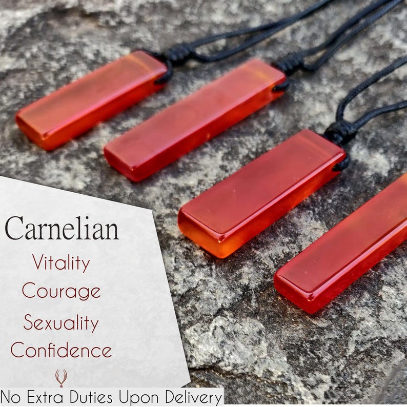 Four polished, elongated, rectangular Carnelian crystal necklaces are displayed on a textured gray surface. The orange-red gemstones have a smooth, translucent texture. There are multiple pendants, each attached to a black cord. Text on the image identifies the stone as "Carnelian" and lists its associated qualities: "Vitality", "Courage", "Sexuality", and "Confidence".