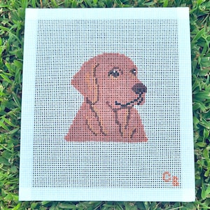 May include: A square needlepoint canvas featuring a brown dog portrait centered on a white grid background. The dog has dark eyes, a black nose, and floppy ears. The initials CB are stitched in orange in the bottom right corner of the canvas.