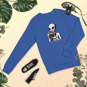 May include: Royal blue sweatshirt featuring a black and white illustration of an alien holding a camera. The text "Say Zeeeezays!" is below the alien. Black and white sneakers and a camera are also in the image.