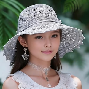 May include: A light gray, open-weave sun hat with a wide brim. The hat features a delicate, lacy pattern and a small bow detail. The brim has a scalloped edge. The hat is worn with matching earrings and a necklace.