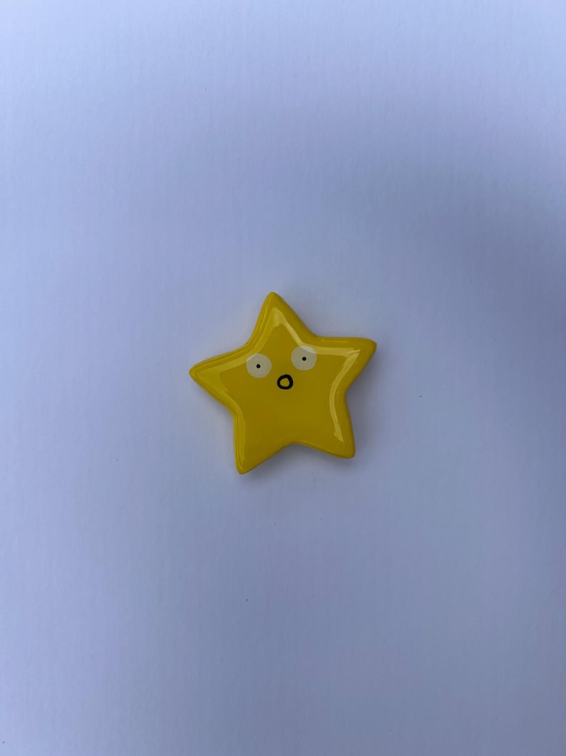 K&ouml;nnte beinhalten: Ein leuchtend gelbes, sternf&ouml;rmiges Objekt mit einer glatten, gl&auml;nzenden Oberfl&auml;che. Der Stern hat ein einfaches, handgezeichnetes Gesicht, bestehend aus zwei wei&szlig;en, kreisf&ouml;rmigen Augen mit schwarzen Pupillen und einem kleinen schwarzen Mund.