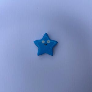 K&ouml;nnte beinhalten: Ein leuchtend blaues, sternf&ouml;rmiges Objekt mit einer glatten, gl&auml;nzenden Oberfl&auml;che. Der Stern hat ein einfaches aufgedrucktes Gesicht, bestehend aus zwei wei&szlig;en, kreisf&ouml;rmigen Augen mit schwarzen Pupillen und einem kleinen, geschwungenen Mund.