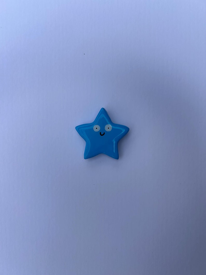 K&ouml;nnte beinhalten: Ein leuchtend blaues, sternf&ouml;rmiges Objekt mit einer glatten, gl&auml;nzenden Oberfl&auml;che. Der Stern hat ein einfaches aufgedrucktes Gesicht, bestehend aus zwei wei&szlig;en, kreisf&ouml;rmigen Augen mit schwarzen Pupillen und einem kleinen, geschwungenen Mund.