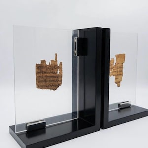 May include: A pair of black wooden bookends with clear acrylic panels. Each panel holds a fragment of ancient parchment with visible text. The bookends have a minimalist design, suitable for displaying historical artifacts.