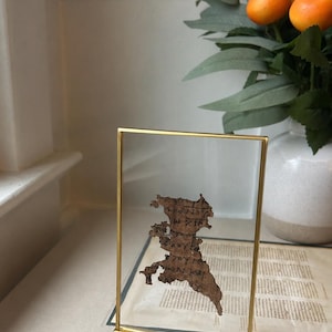 May include: A framed papyrus fragment with Greek text from Revelation 13:18, displayed in a gold-colored frame. The text reads "let the one who has understanding calculate the number of the beast... it is 616." The frame sits on a white surface.