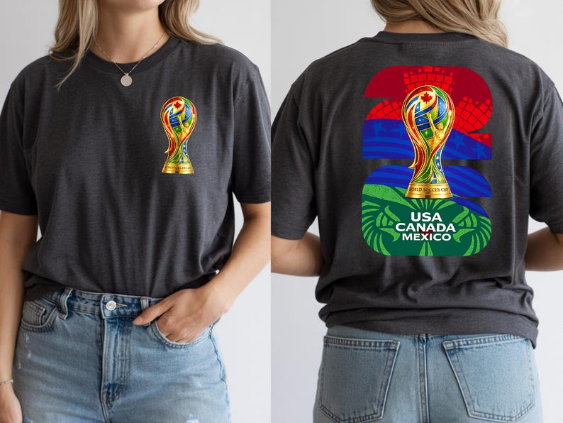 May include: Dark gray t-shirt featuring a gold trophy with colorful accents on the front and back. The back design includes the text "USA CANADA MEXICO" and the number "26". The shirt is made of a soft material.