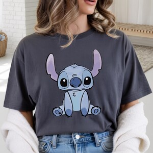 Puede incluir: Camiseta gris oscuro con una ilustraci&oacute;n de dibujos animados de Stitch, un extraterrestre azul con orejas y ojos grandes. El gr&aacute;fico est&aacute; centrado en la camiseta. La camiseta est&aacute; hecha de un material suave.