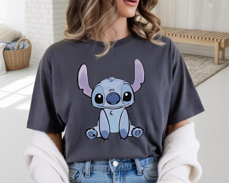 Puede incluir: Camiseta gris oscuro con una ilustraci&oacute;n de dibujos animados de Stitch, un extraterrestre azul con orejas y ojos grandes. El gr&aacute;fico est&aacute; centrado en la camiseta. La camiseta est&aacute; hecha de un material suave.
